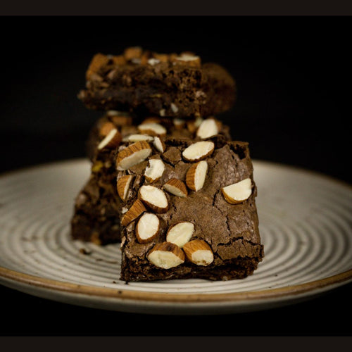 Chocolate brownies topped with almonds on a white plate against a dark background.