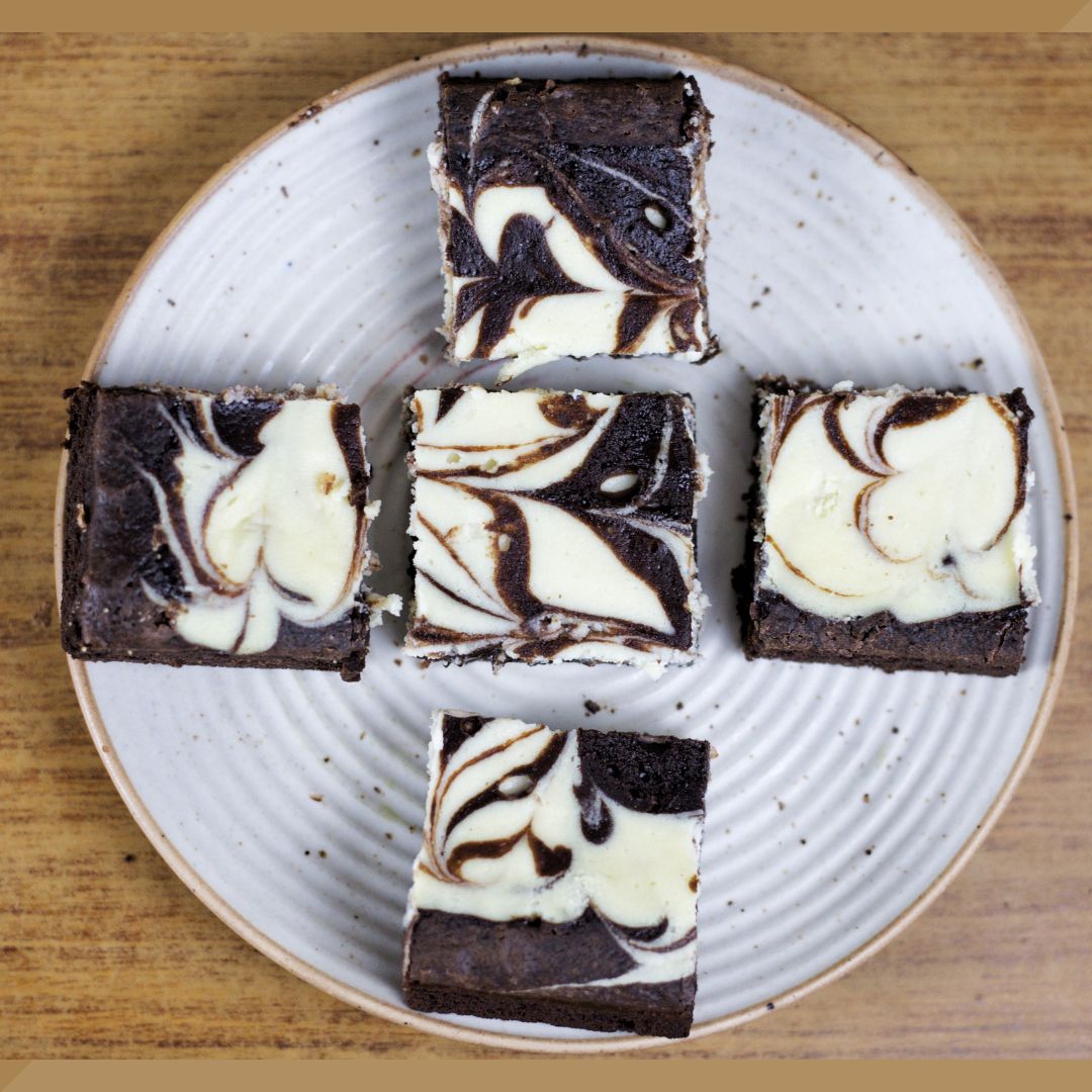 Cheesecake swirled brownies on a white plate with a wooden background.