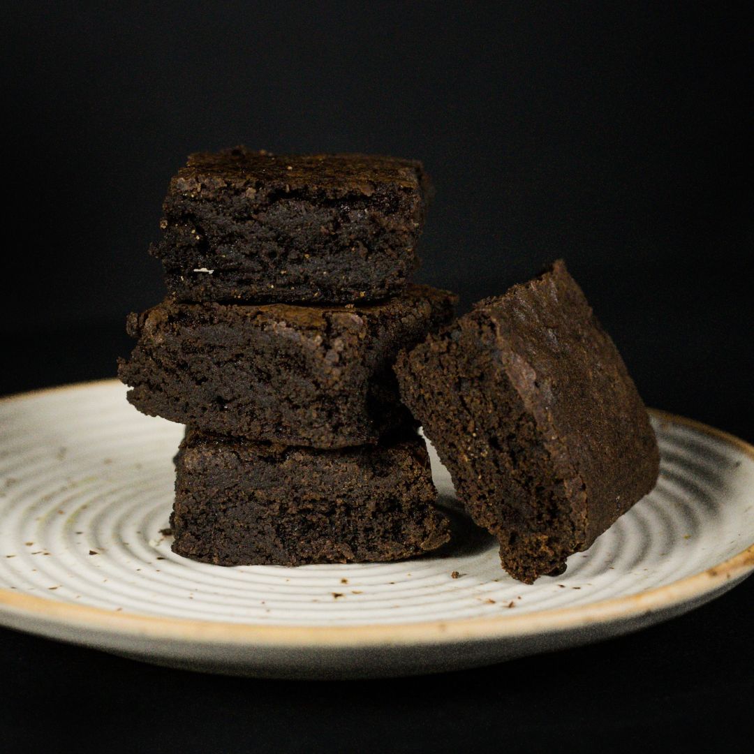 Stack of dark chocolate brownies on a white plate with a black background.
